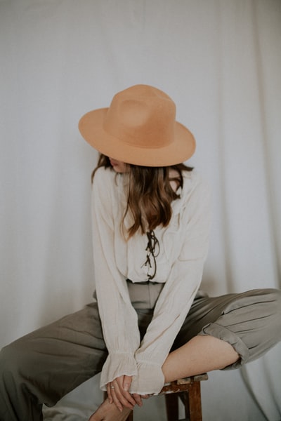 穿着白色长袖衬衫和灰色裤子，头戴棕色软呢帽的女人坐在床上